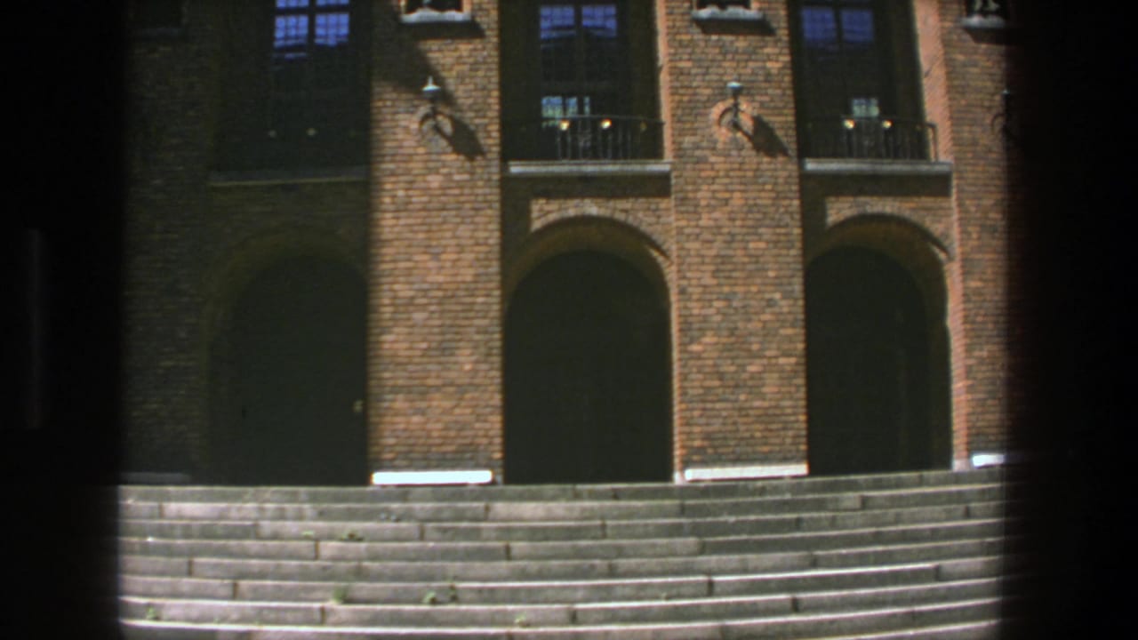 Brick entrance facade with stairs, dark arches and upper windows.
