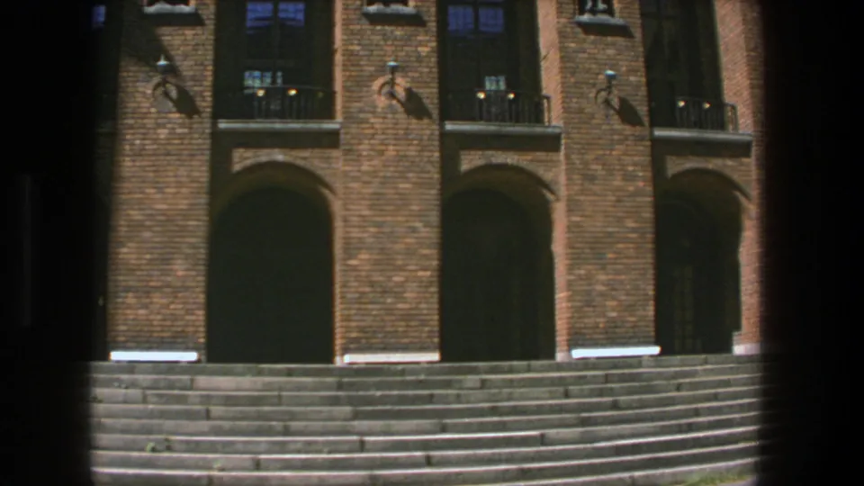 Final 8mm frame of the Stockholm university entrance, centered on brick arches, dark doorways, upper windows and stone stairs.