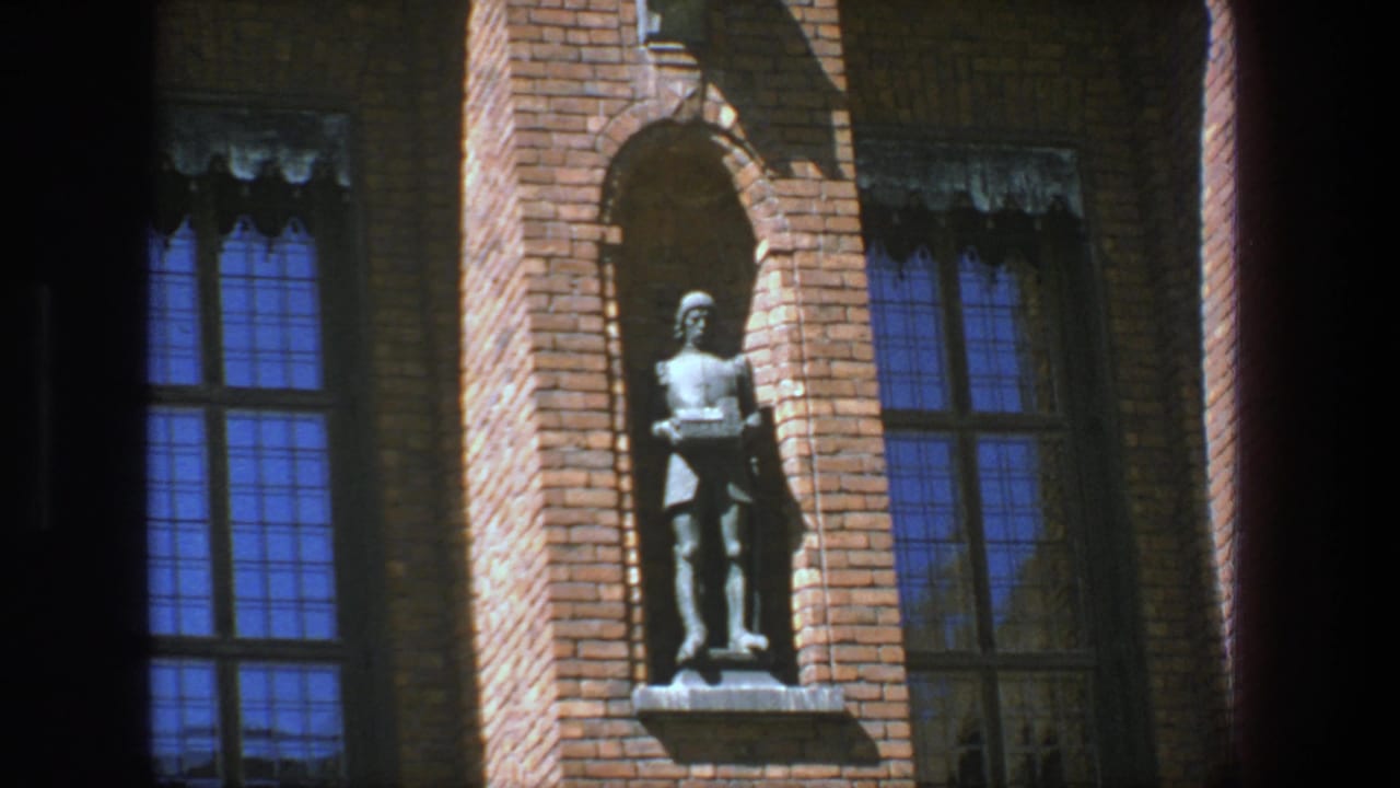 Religious sculpture in a brick niche beside tall blue windows.