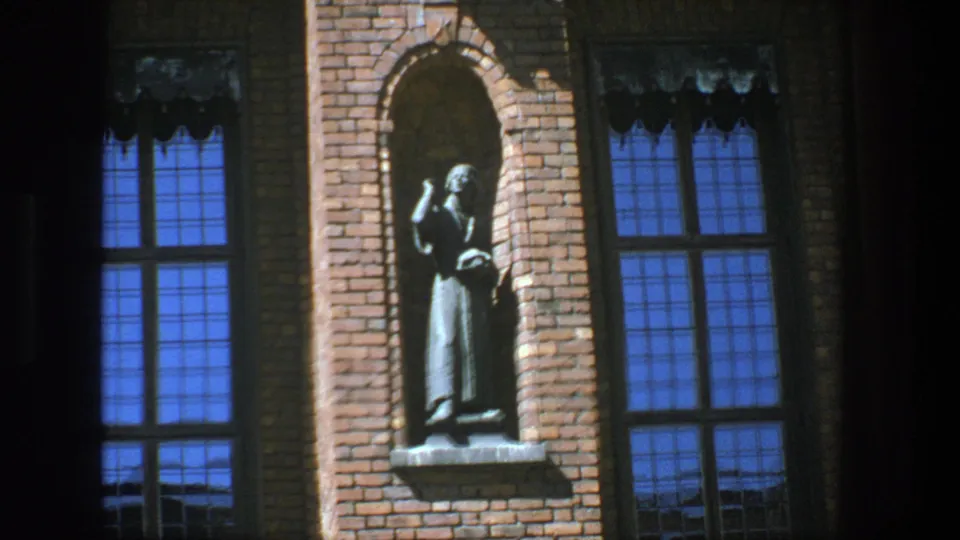 1975 Stockholm facade detail with a robed religious figure in a brick niche, framed by tall blue-reflecting windows.
