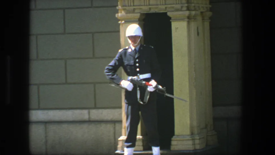 1975 Stockholm frame of a ceremonial guard standing rigidly at a formal stone entrance, rifle and bayonet visible.