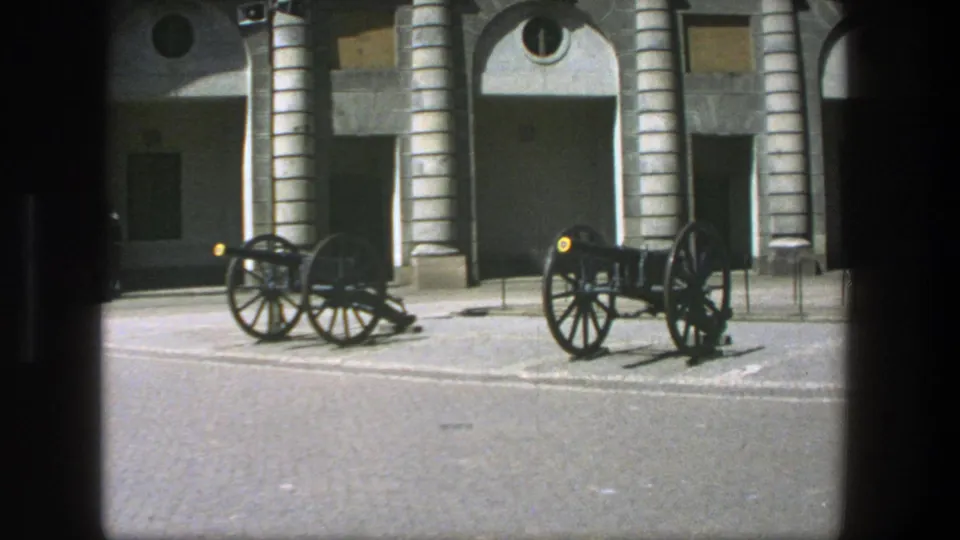 1975 Stockholm 8mm view of paired black cannons on a courtyard, with arched stone bays and circular windows behind them.