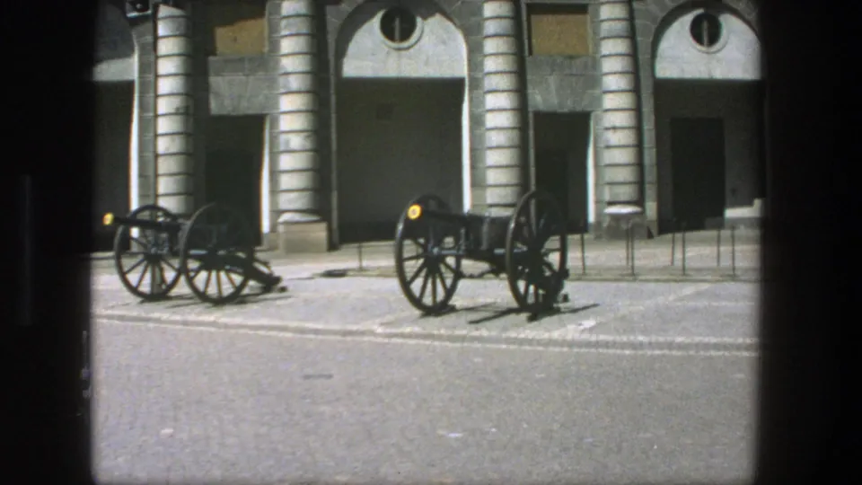 Stockholm 1975 home-movie still with two black cannons, cobbled paving, and a tan arched stone building in soft 8mm color.