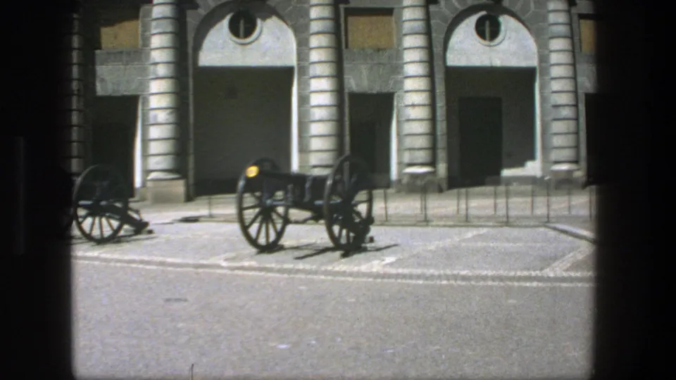Late clip frame from 1975 Stockholm showing a black cannon near center and another partly visible beside arched stone architecture.