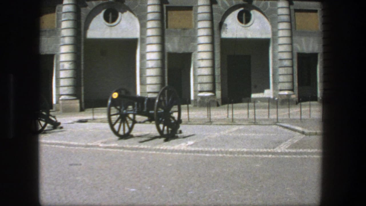 Cannon on pavement in front of arched stone building facade.