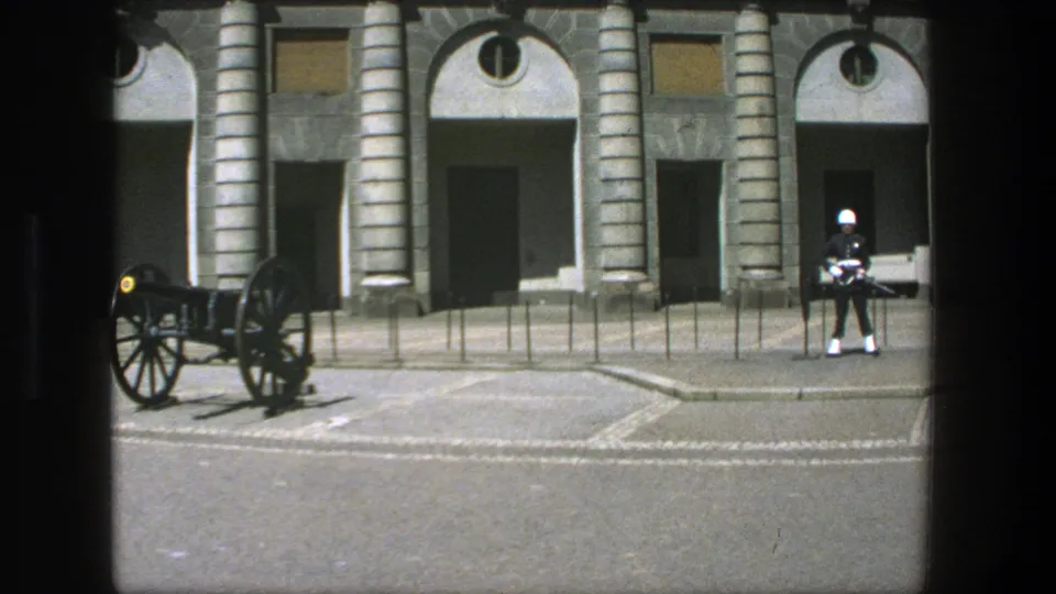 1975 Stockholm frame with a ceremonial soldier in white helmet and dark uniform standing near a cannon outside a historic building.
