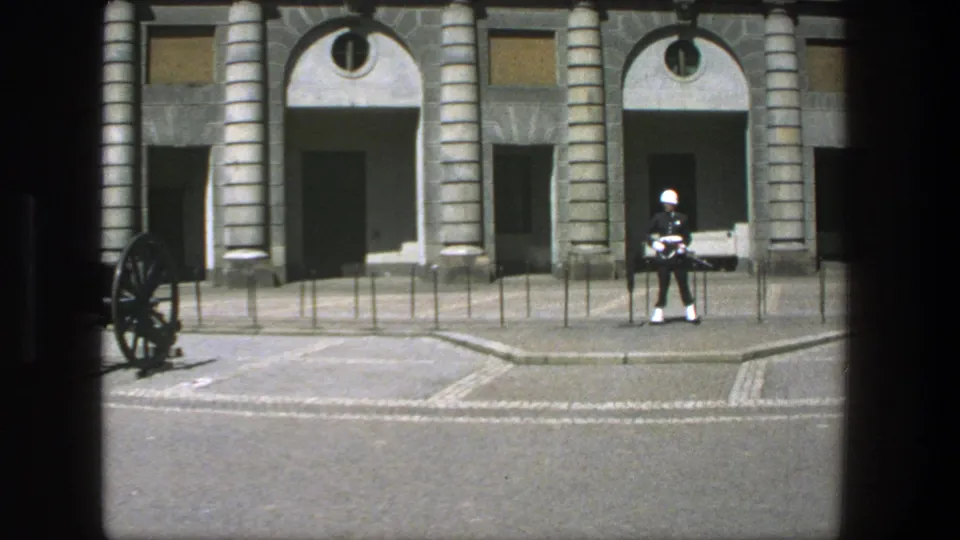 1975 Stockholm 8mm frame showing a ceremonial soldier with rifle in front of arched doorways and stone columns.