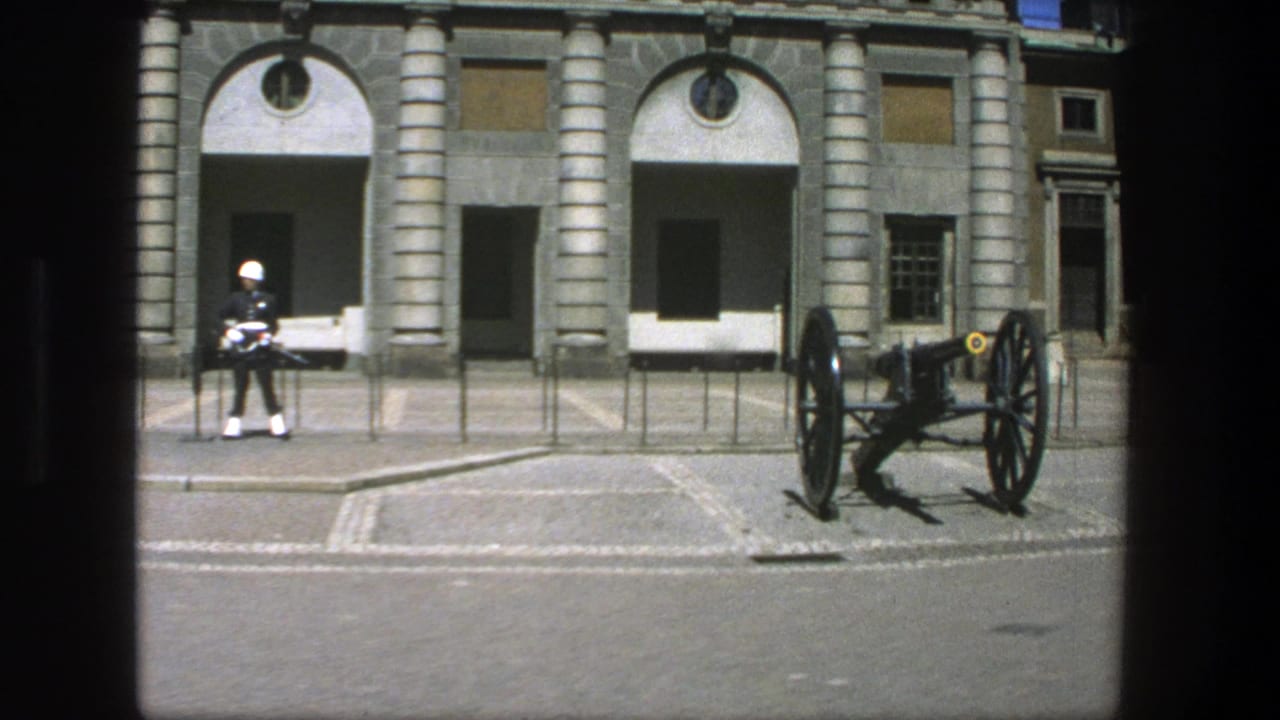 1975 Stockholm 8mm frame showing a white-helmeted guard near a displayed cannon in front of a formal stone facade.