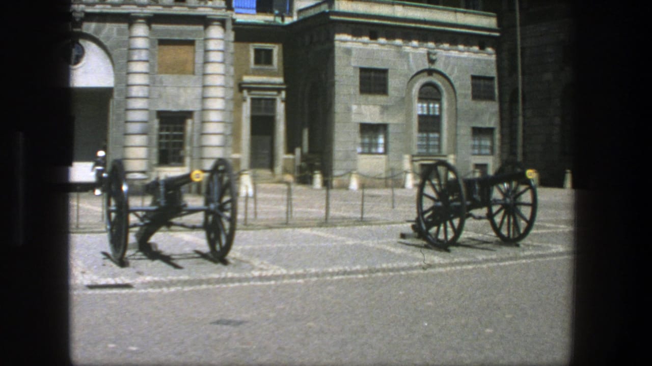 1975 Stockholm 8mm frame showing a paved courtyard, two displayed cannons and a stone building with columns and arched windows.