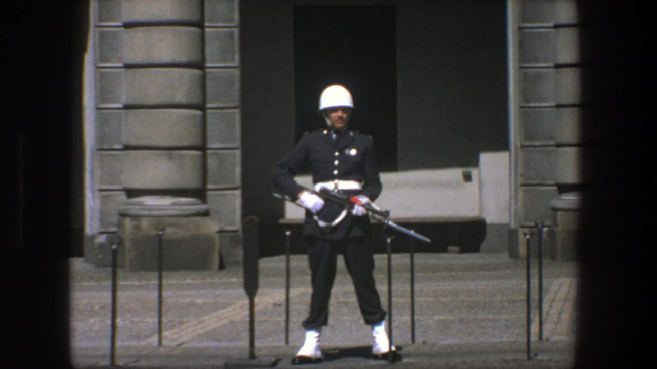 Uniformed guard with white helmet standing outside a stone building entrance.