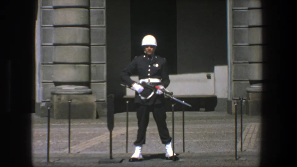 1975 Stockholm 8mm frame with a dark-uniformed guard holding a rifle with bayonet before a formal stone entrance.