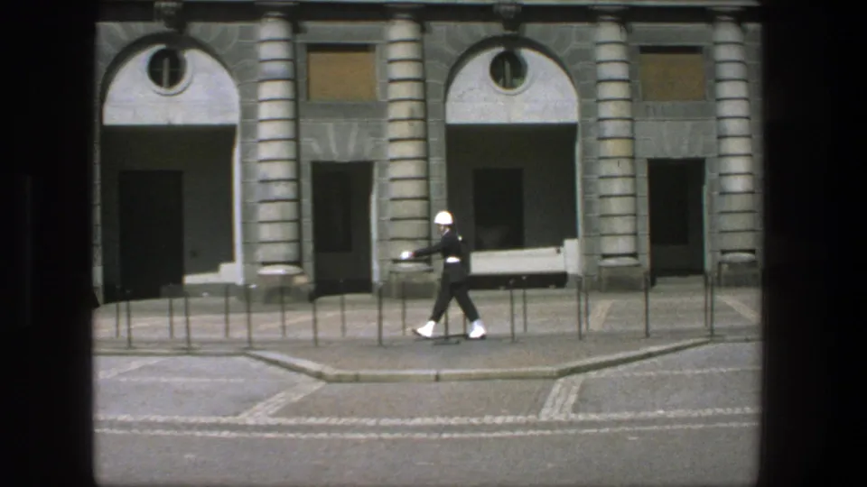 The guard continues a measured march across the Stockholm street scene, framed by columns and arched doorways.