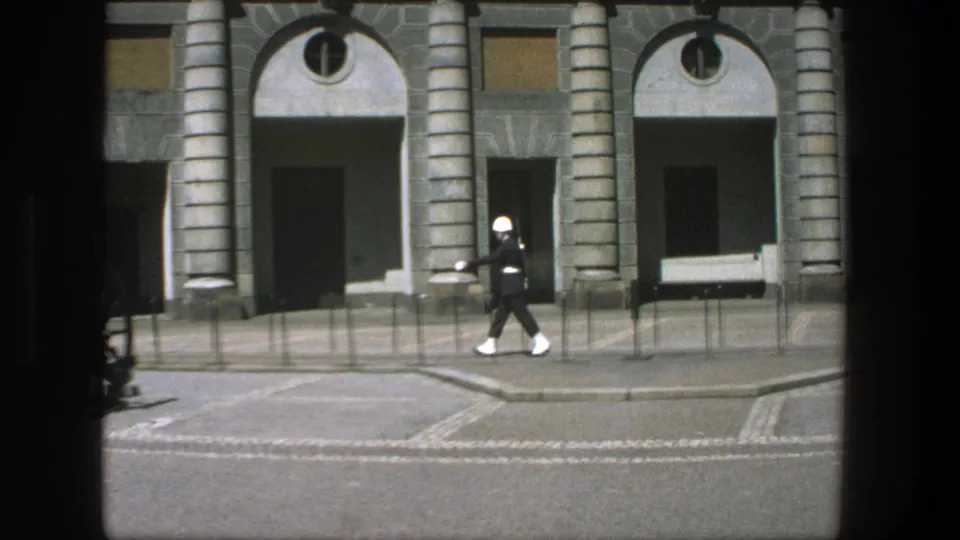 A uniformed guard in white boots passes in front of the arched stone building in the 1975 Stockholm footage.
