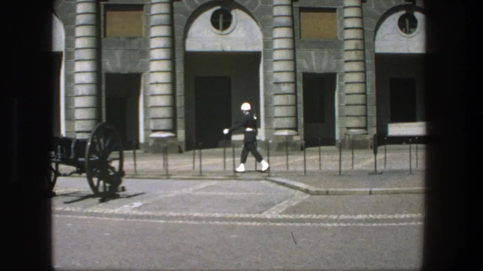 The guard marches past the building as a cannon appears in the foreground of the Stockholm home-movie view.