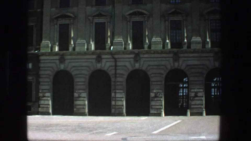1975 Stockholm 8mm frame showing arched doorways, stonework, and a Swedish flag above the roofline.