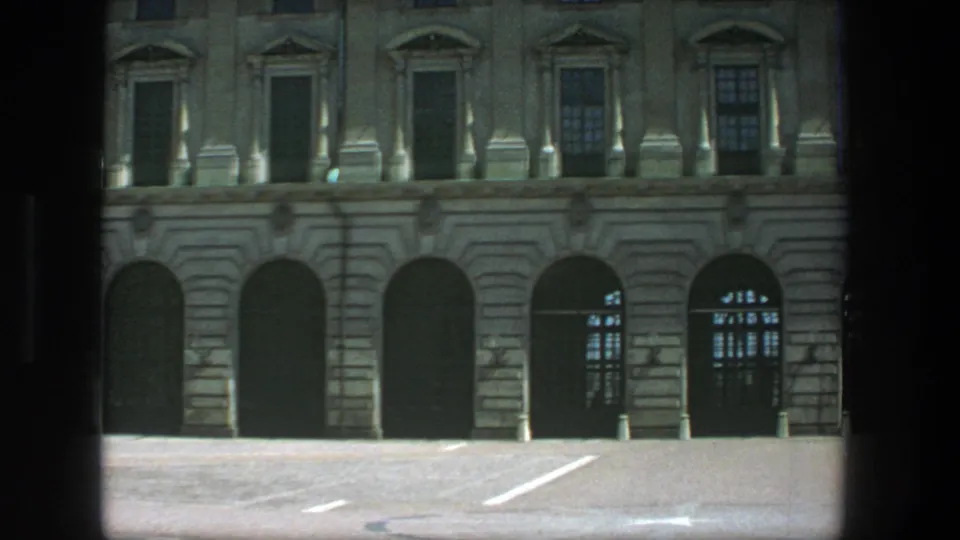 Stockholm 8mm frame with a Swedish flag over a formal stone facade, arched entrances, and bright blue sky.