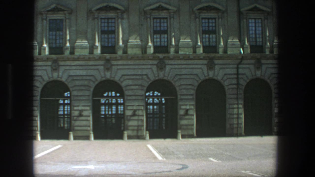 Classical stone building facade across an empty marked parking lot.