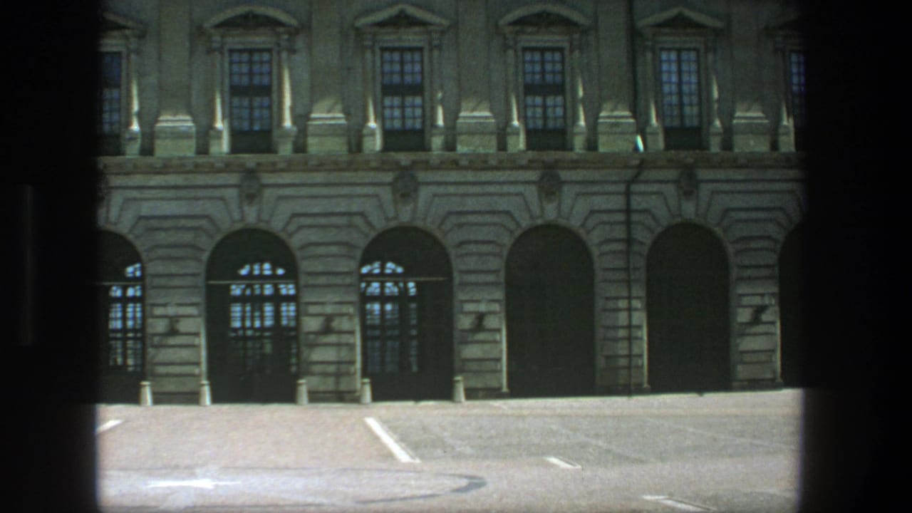Stockholm building exterior on 8mm film, showing arched entries, upper windows, bollards, and a quiet empty lot.