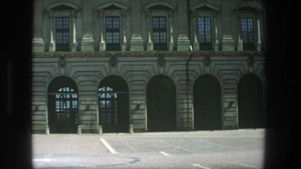 1975 Stockholm exterior with a classical stone facade, arched windows and doors, white lot markings, and soft 8mm grain.