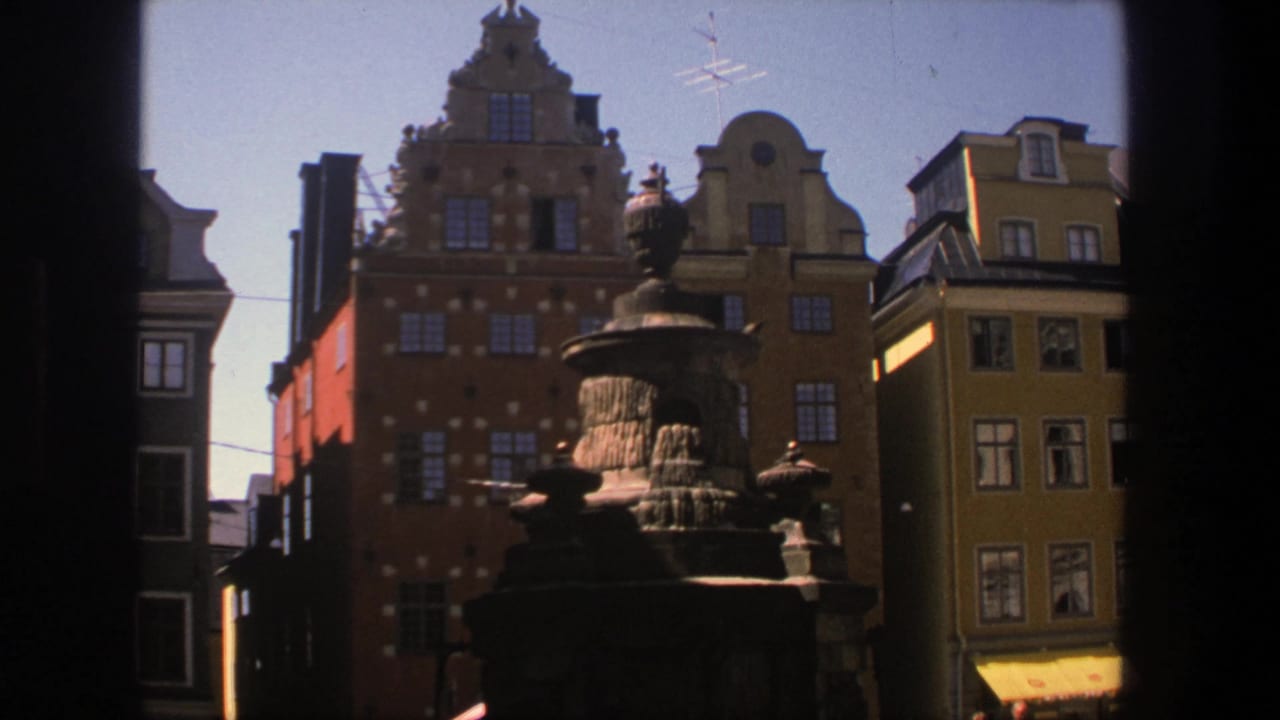 Fountain and tall colorful buildings seen through a dark central window edge.