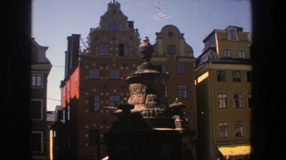 Stockholm streetscape on 8mm film, with a fountain in front of red, yellow, and brown gabled facades.