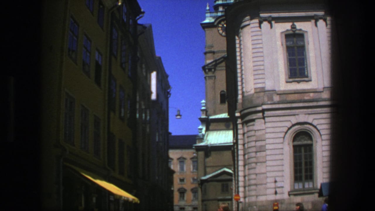 Stockholm street view from 1975 showing pedestrians near a pale historic building, dark adjoining facades, copper roof details, and clear sky.