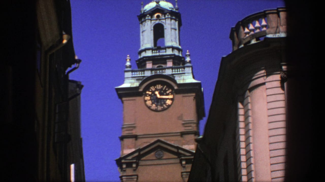 1975 Stockholm 8mm frame showing an ornate clocktower with Roman numerals seen from a narrow street below.