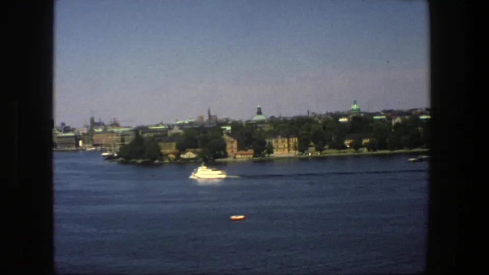 Final Stockholm harbor frame with the white boat near the far shore and a small orange craft or buoy visible on the blue water.