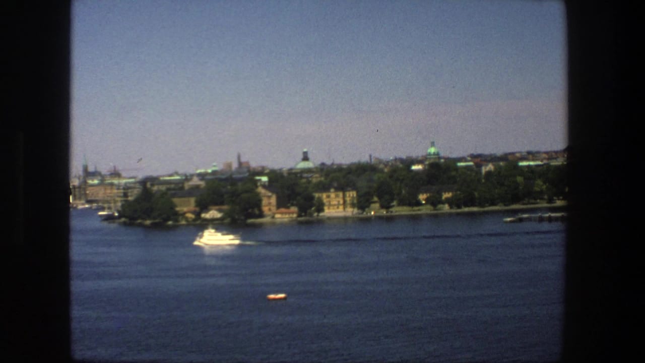 White boat crossing water below a distant Stockholm shoreline and skyline.