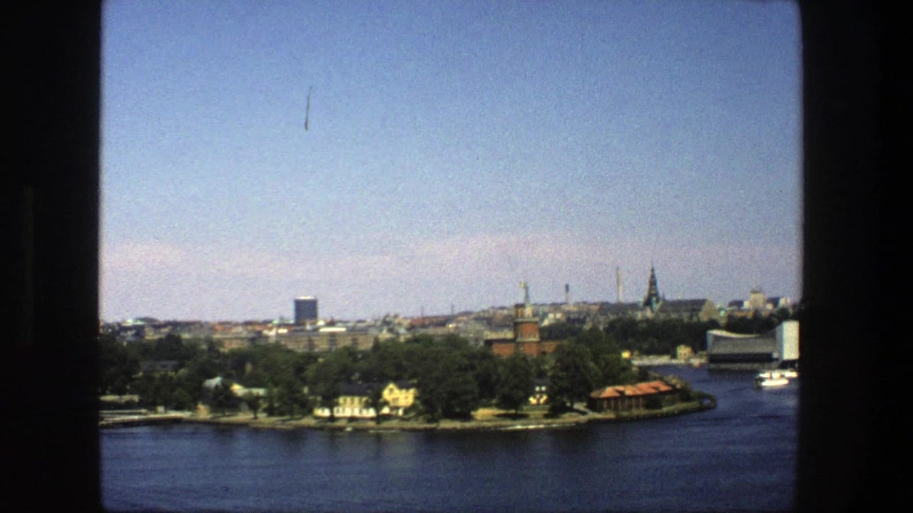 Distant Stockholm skyline across water with wooded shoreline and blue sky.