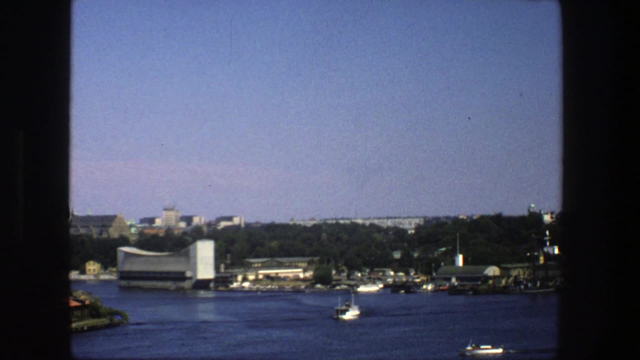 Wide water view with shoreline buildings, trees, and small boats.