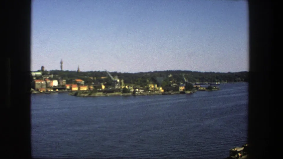 Stockholm's distant waterfront remains framed by dark edges, with rippled water in the foreground and buildings, cranes, trees, and a tower beyond.