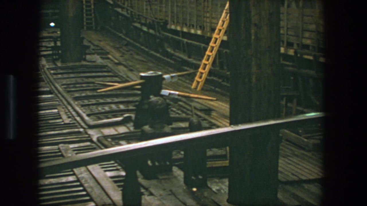 1975 Stockholm 8mm frame showing a dim industrial tunnel with rail tracks, heavy wood structure, a metal railing, and a yellow ladder.