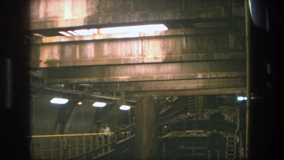 1975 Stockholm 8mm frame showing a distant man on a raised walkway beneath overhead lights in a large industrial tunnel.