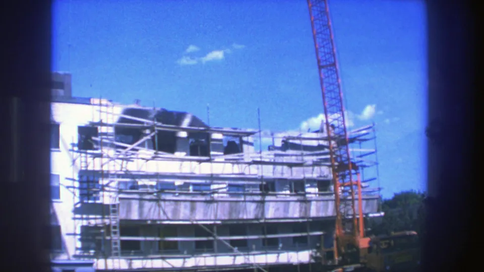 1975 Stockholm 8mm exterior view of an unfinished building with scaffolding and a tall red crane against blue sky.
