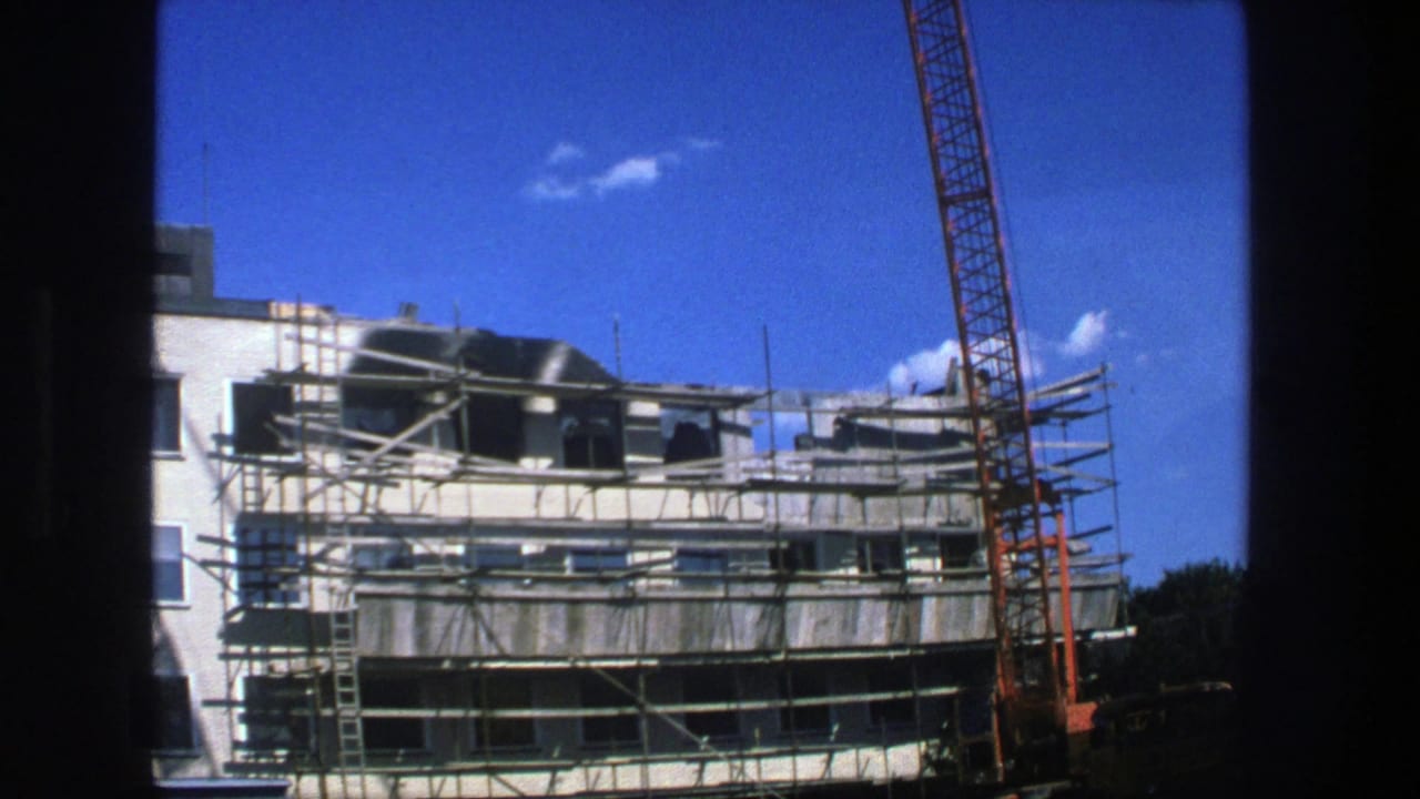 Scaffolded building facade with an orange crane against a blue sky.