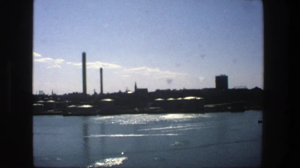 1975 Stockholm 8mm frame with a silhouetted industrial shoreline, calm reflective water, and dark film-frame edges.