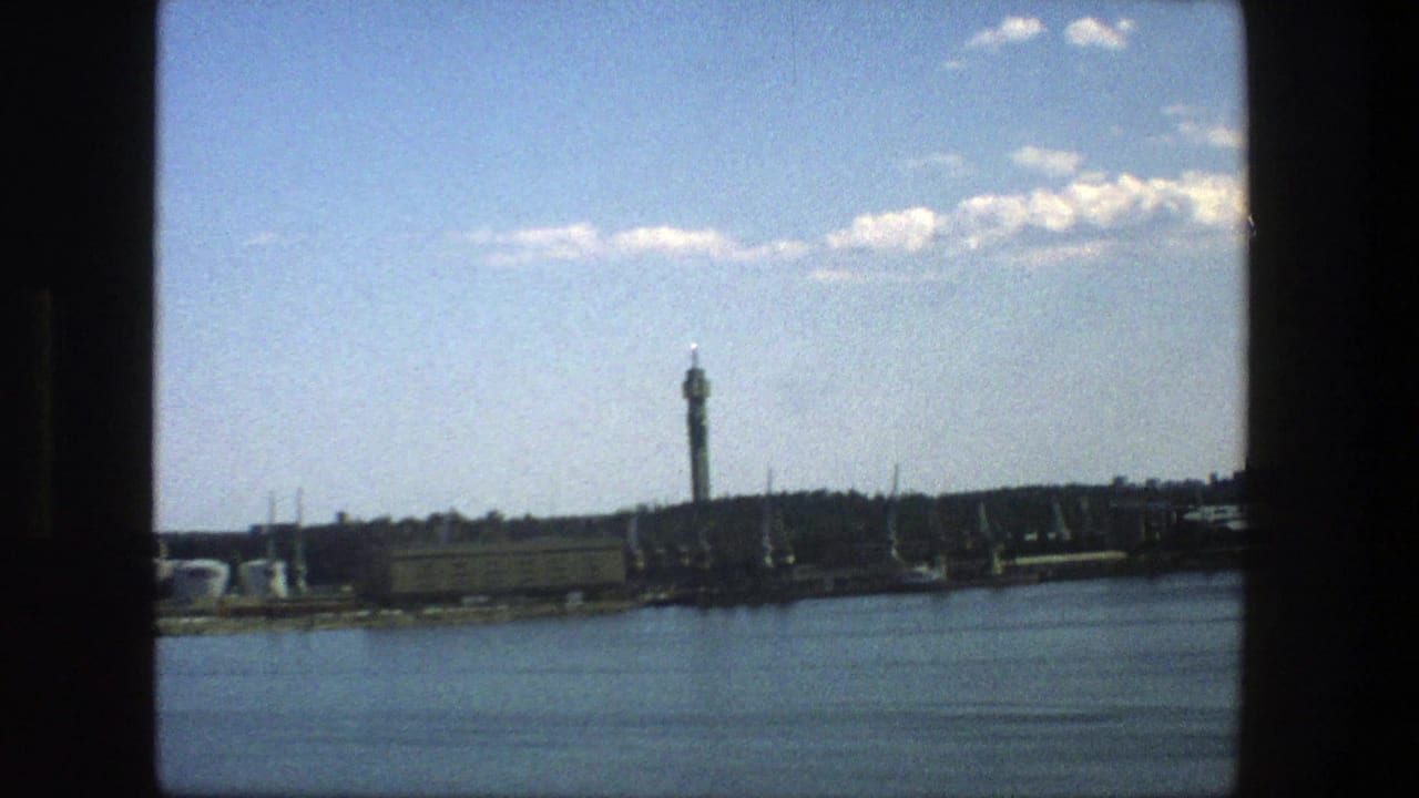 1975 Stockholm home-movie view of a tall waterfront tower seen across calm water through dark frame edges.