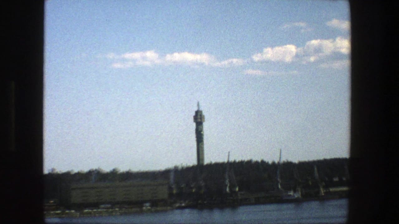 1975 Stockholm waterfront tower framed more tightly, with cranes and low buildings along the riverbank.