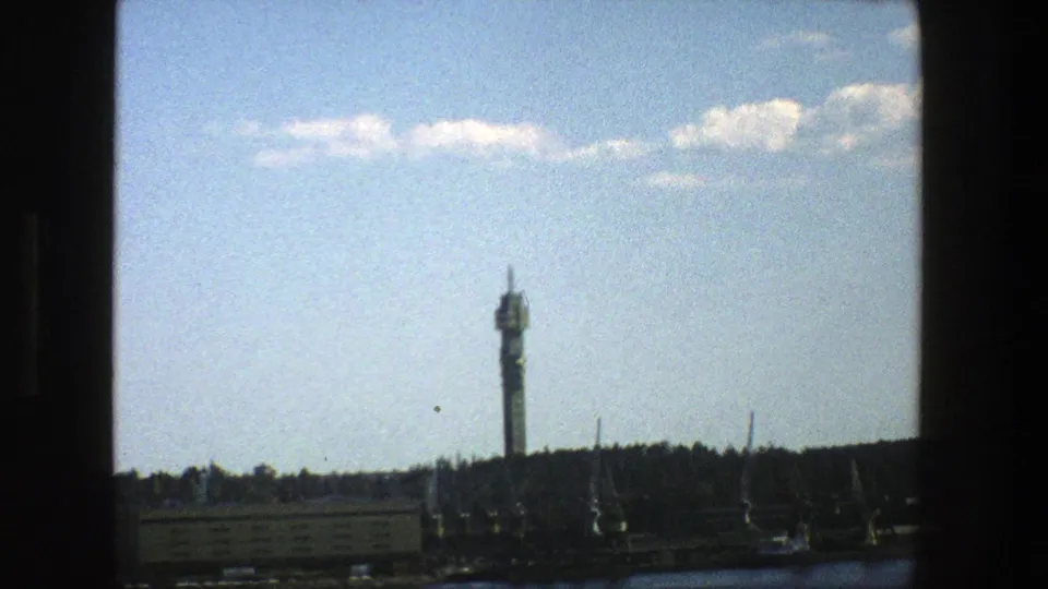 Final 1975 Stockholm frame holds on the tower, cranes, low buildings, and riverfront under scattered clouds.