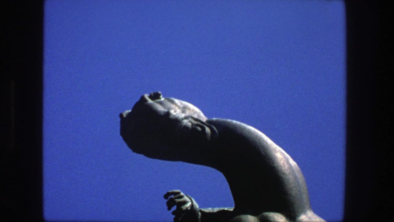 1975 Stockholm 8mm frame showing a dark, weathered abstract statue head and curved neck against clear blue sky.