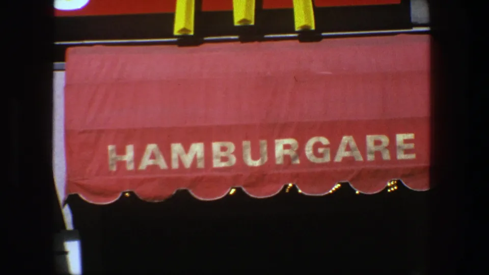 Close view of a red HAMBURGARE awning in 1975 Stockholm home-movie footage.