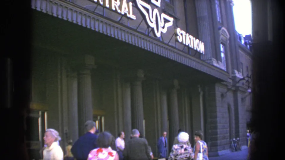 Crowd at the Stockholm Central Station entrance beneath illuminated signage in 1975 footage.