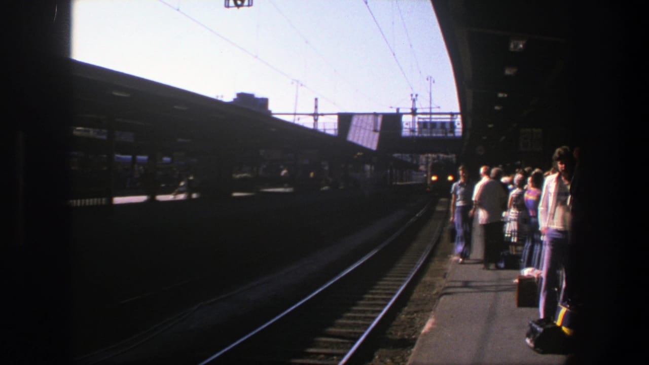 Sunlit 1975 Stockholm rail platform seen from track level, with passengers and luggage at the edge.