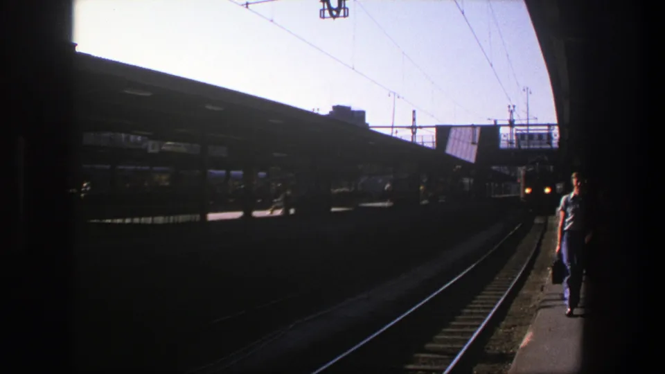 1975 Stockholm station view with tracks, overhead lines, dark canopy shadows, and a traveler at frame edge.