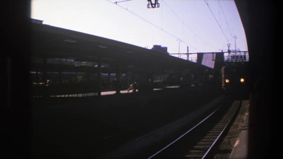 1975 Stockholm 8mm frame showing an electric train approaching a dark station platform under overhead catenary wires.