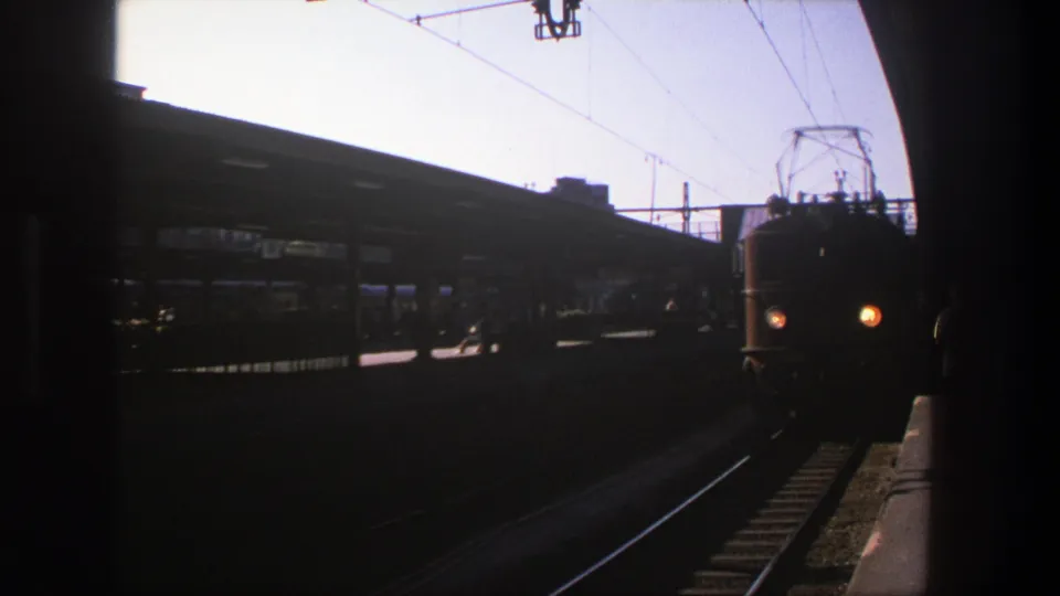 1975 Stockholm 8mm frame of an electric train nearing the camera, with pantograph and station canopy visible.