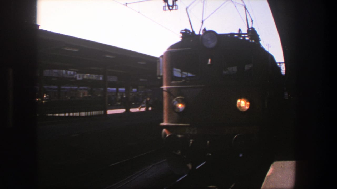 1975 8mm frame of a yellow passenger train approaching a Stockholm station platform in daylight.