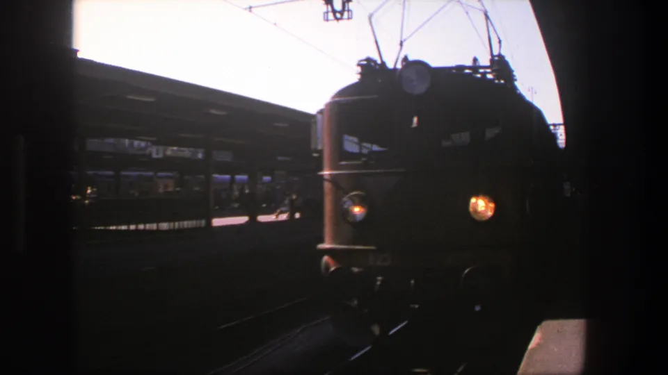 1975 8mm frame of a yellow passenger train approaching a Stockholm station platform in daylight.