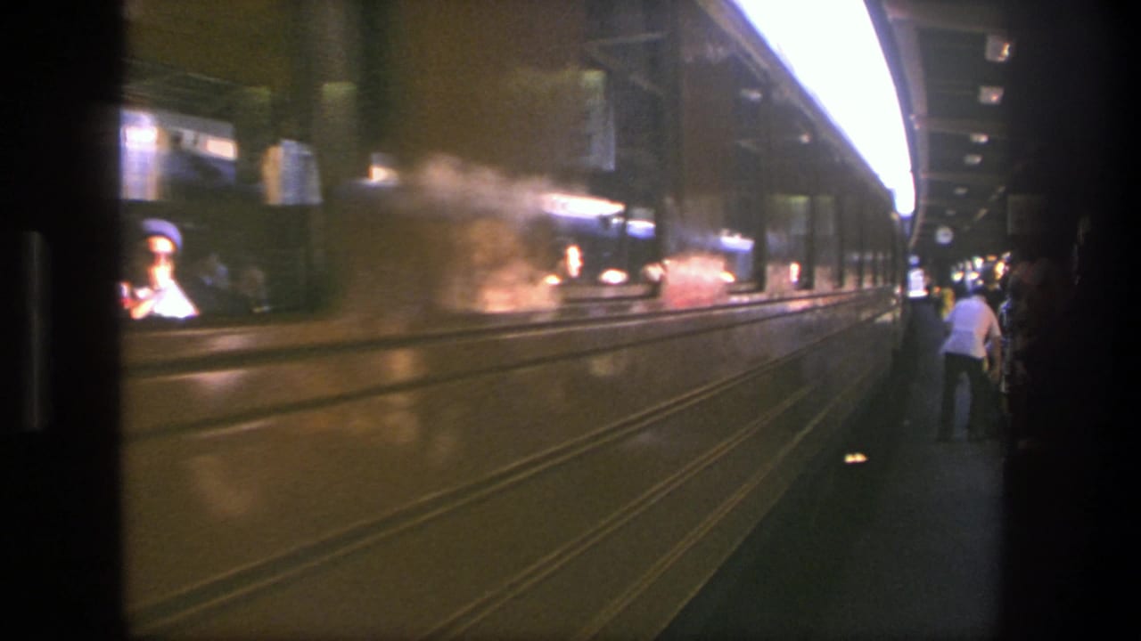 Subway platform seen from a train window with a passing train and passengers nearby.